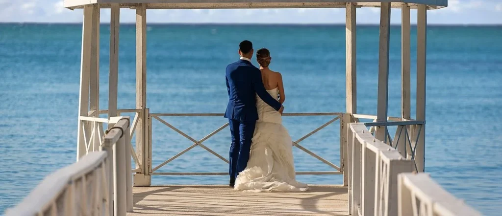 A couple standing at the end of a white pier gazebo overlooking the Caribbean at Grand Palladium Jamaica