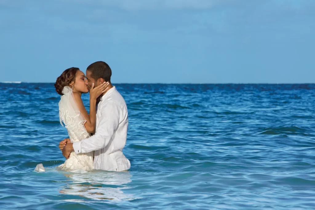 A couple in wedding dress and white shirt embrace in the turquoise Caribbean sea off the beach at Dreams Sapphire Resort and Spa in Puerto Morelos, Mexico
