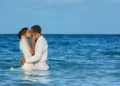 A couple in wedding dress and white shirt embrace in the turquoise Caribbean sea off the beach at Dreams Sapphire Resort and Spa in Puerto Morelos, Mexico