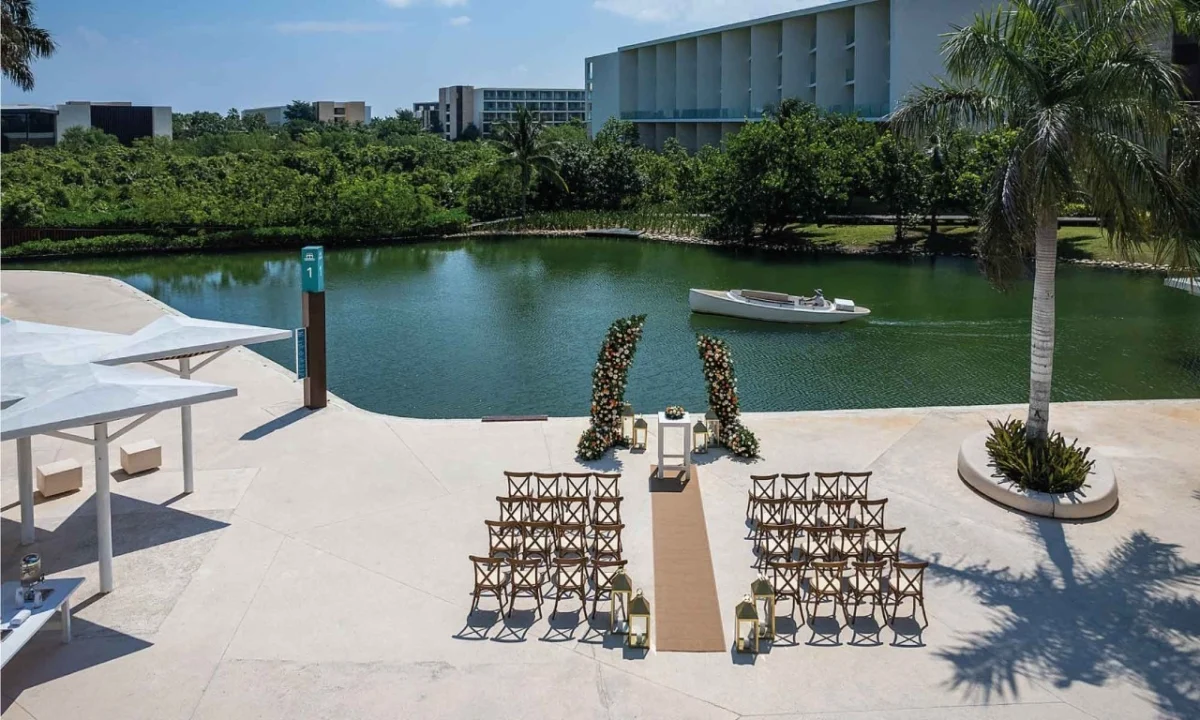 Waterside ceremony setup with roughly fifty chairs and a floral arch at Grand Palladium Costa Mujeres