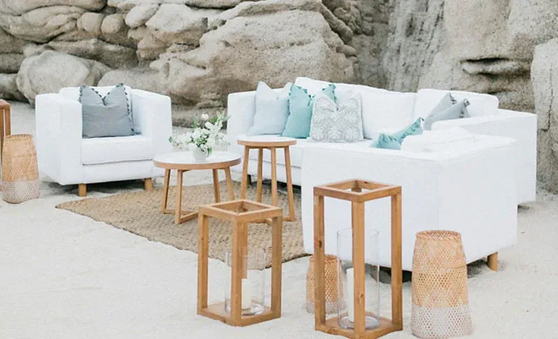 White lounge sofas and woven lanterns arranged on the sand against the granite rock formations at Grand Velas Los Cabos