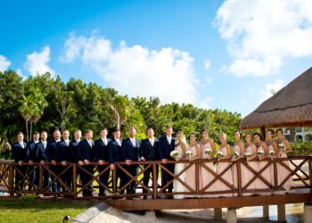 A bride and groom in a navy suit embrace on a wooden bridge framed by palms at The Grand at Moon Palace Cancun