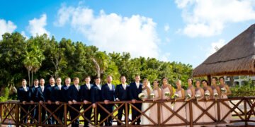 A bride and groom in a navy suit embrace on a wooden bridge framed by palms at The Grand at Moon Palace Cancun