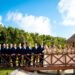 A bride and groom in a navy suit embrace on a wooden bridge framed by palms at The Grand at Moon Palace Cancun