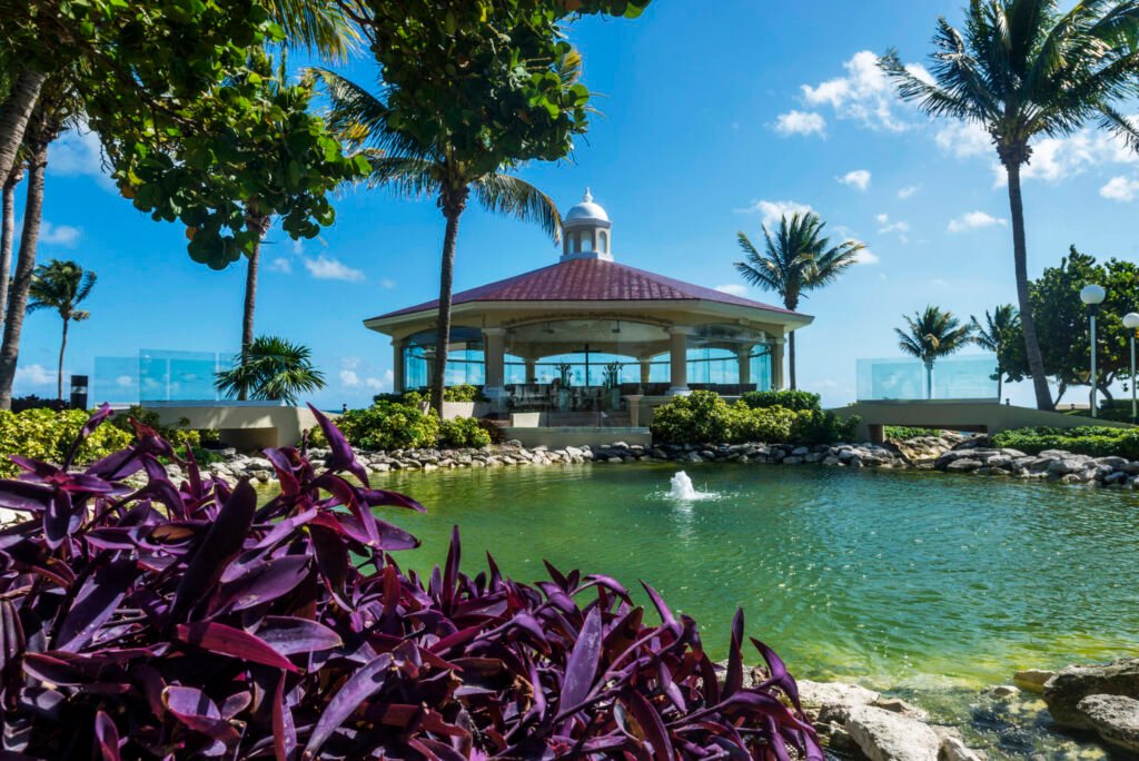 The Chapel of the Immaculate Conception at Moon Palace Cancun, a domed white chapel with a cupola and red tiled roof set beside a landscaped water feature and palm trees