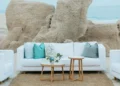 White lounge seating with turquoise and gray pillows on the beach at Grand Velas Los Cabos, set against rock formations and the ocean