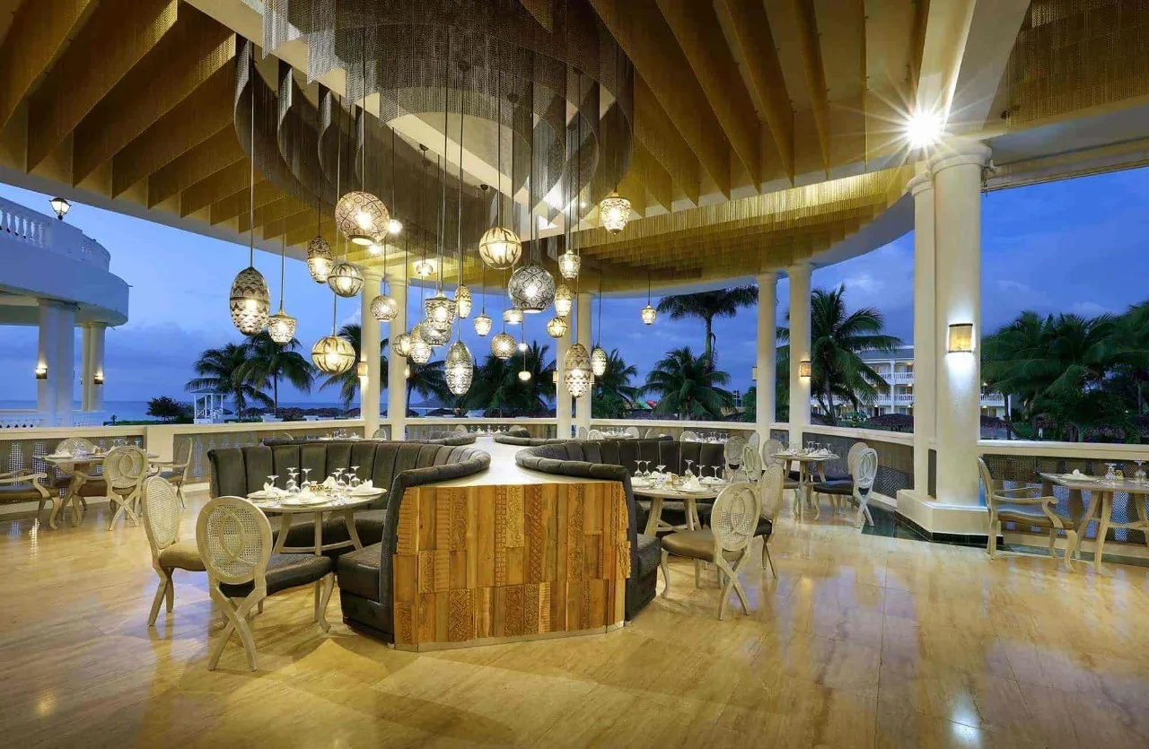 Oceanfront restaurant terrace at dusk at Grand Palladium Jamaica, set with tables under pendant lighting