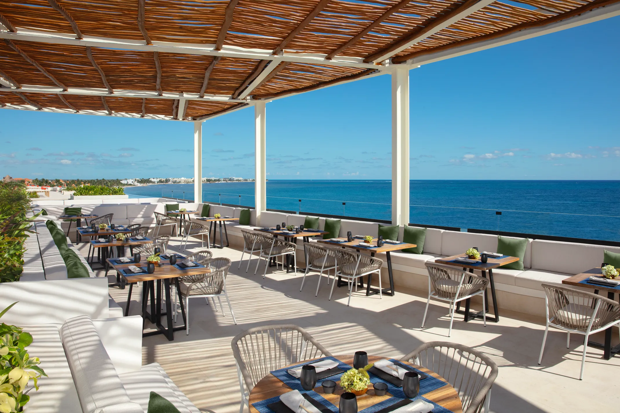 An open-air oceanfront terrace at Dreams Sapphire Resort & Spa with a woven pergola, dining tables and an uninterrupted view of the Caribbean
