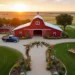Sunset view of a rustic red barn wedding venue in Kansas with floral arch and outdoor seating on green lawn.